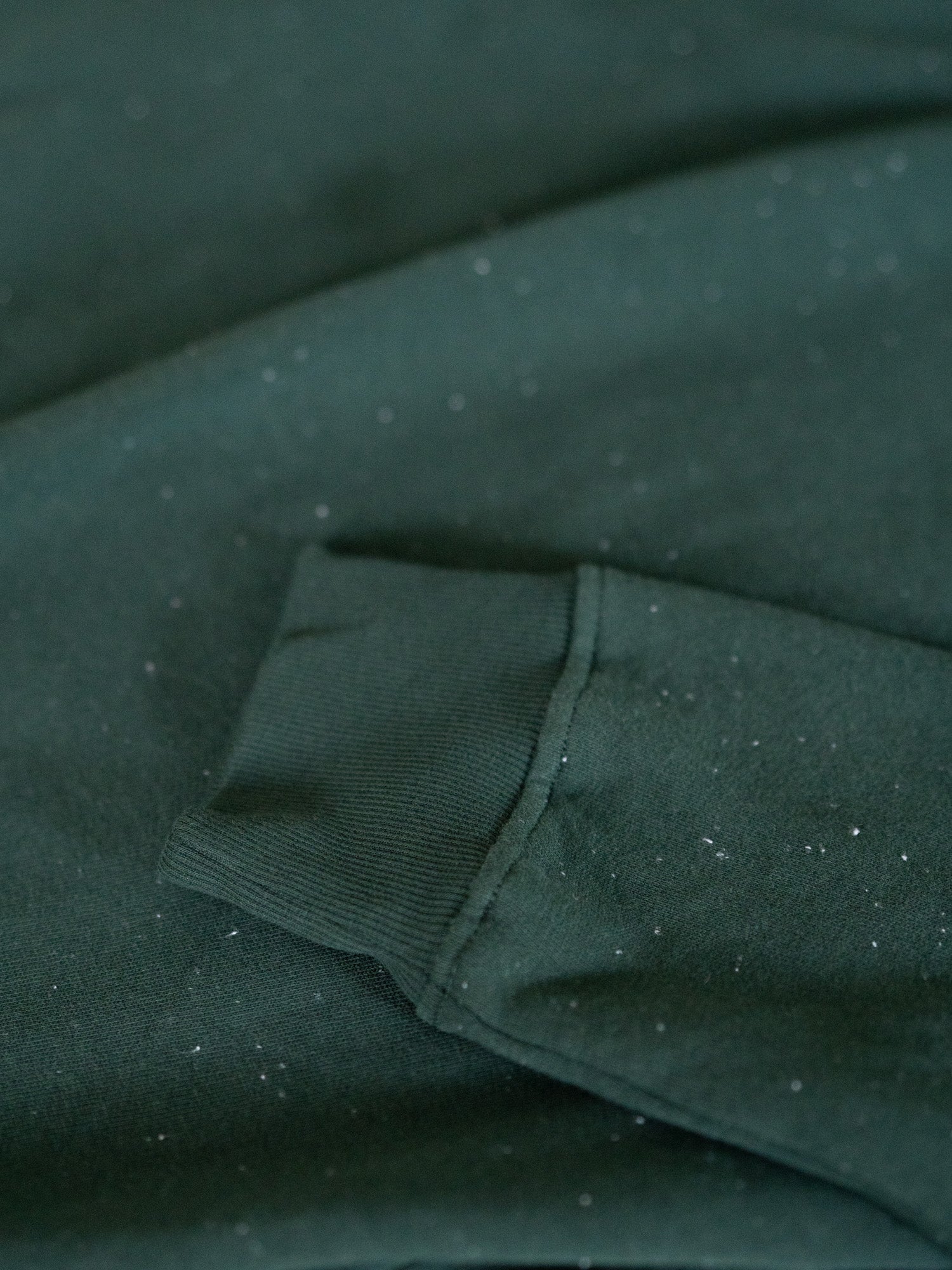 Ärmel-Detail des grünen FUXBAU Neps Pullovers aus Bio-Baumwolle – feine Struktur mit weißen Neps, nachhaltig gefertigt in Portugal