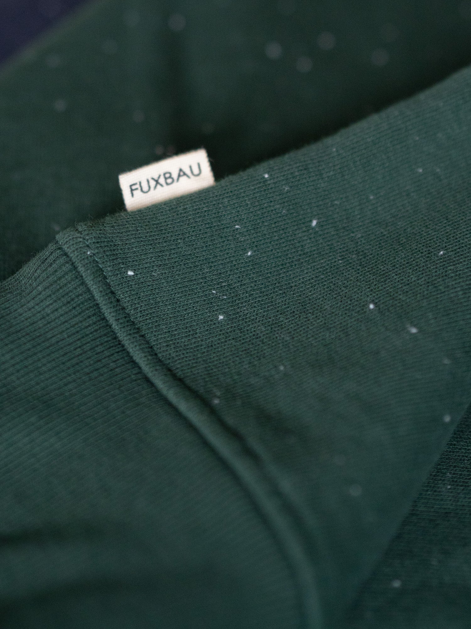 Grüner FUXBAU Neps Pullover aus GOTS-zertifizierter Bio-Baumwolle – Nahaufnahme mit FUXBAU Label und charakteristischer Neps-Oberfläche