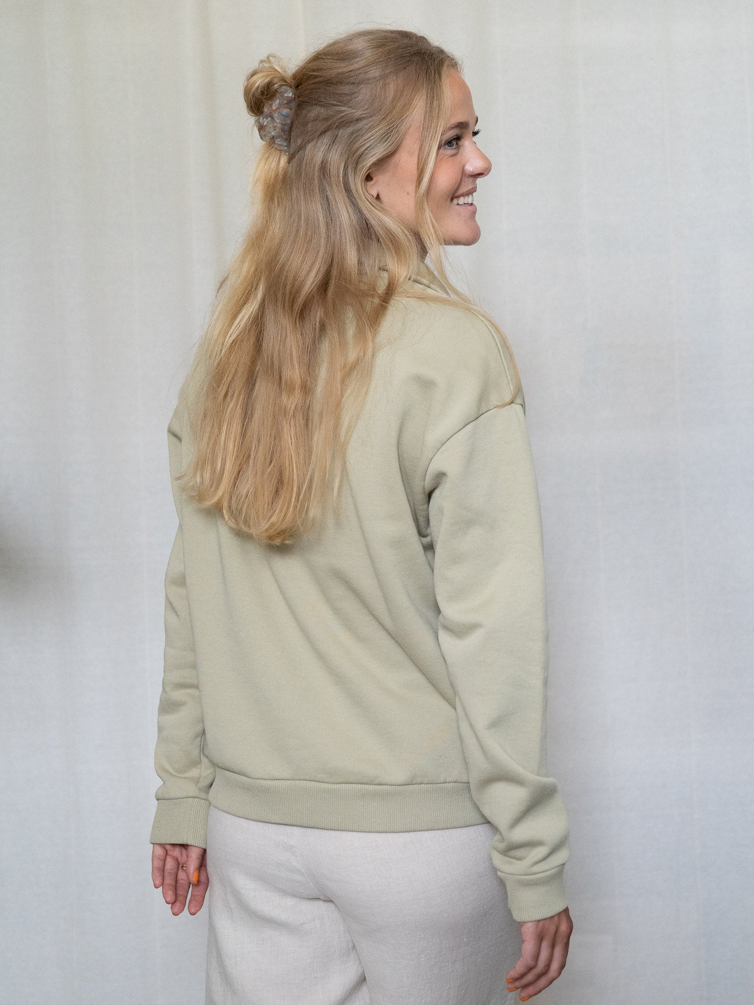 Rückansicht einer Person im salbeifarbenen Half-Zip-Sweater, Haare locker hochgesteckt