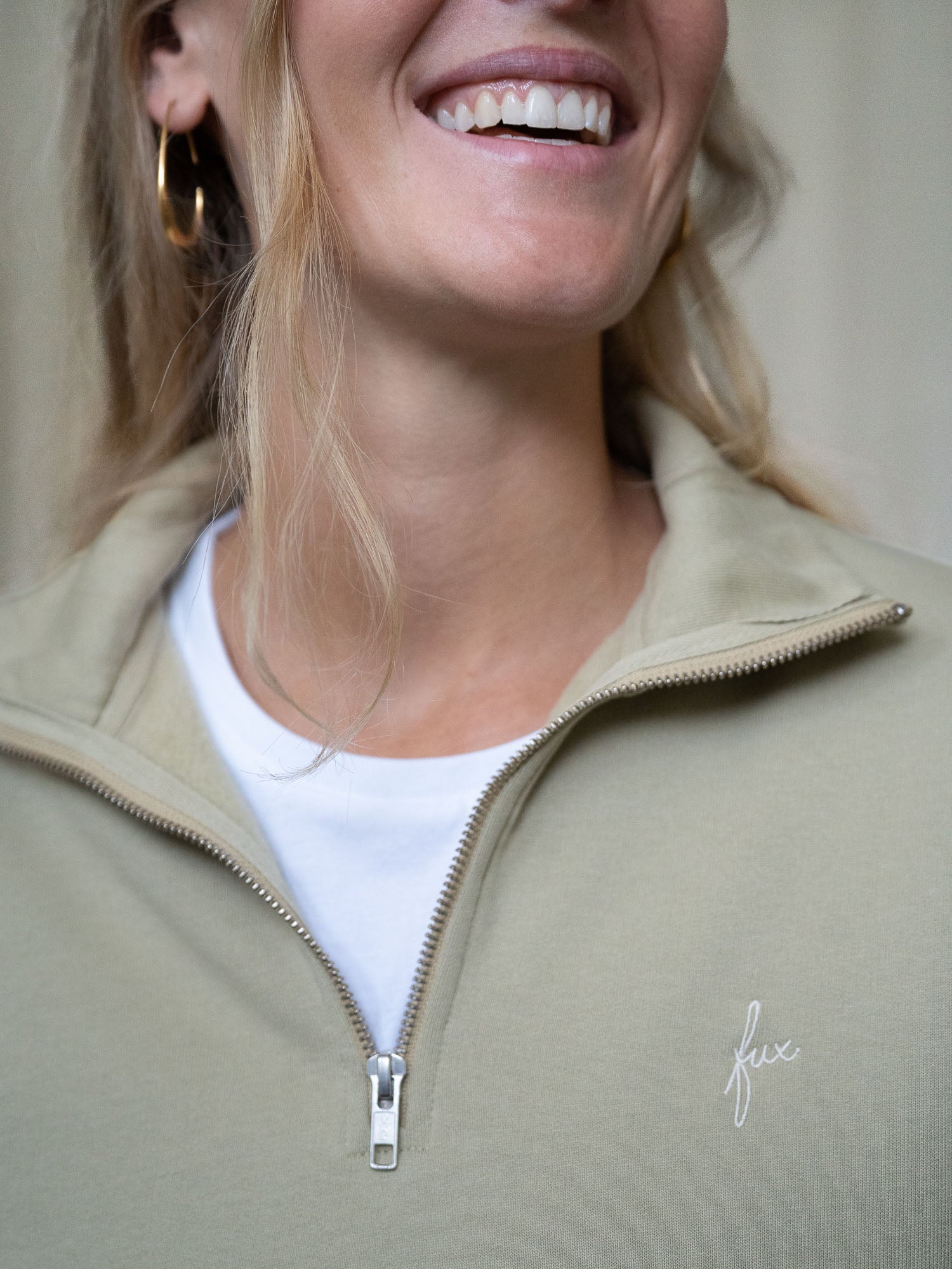 Nahaufnahme des Reißverschlusses und des fux-Sticklogos auf einem salbeifarbenen Half-Zip-Sweater