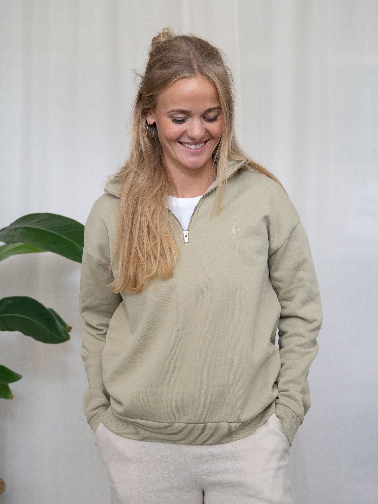 Person mit Händen in den Taschen, trägt salbeifarbenen Half-Zip-Sweater aus Biobaumwolle, Blick nach unten