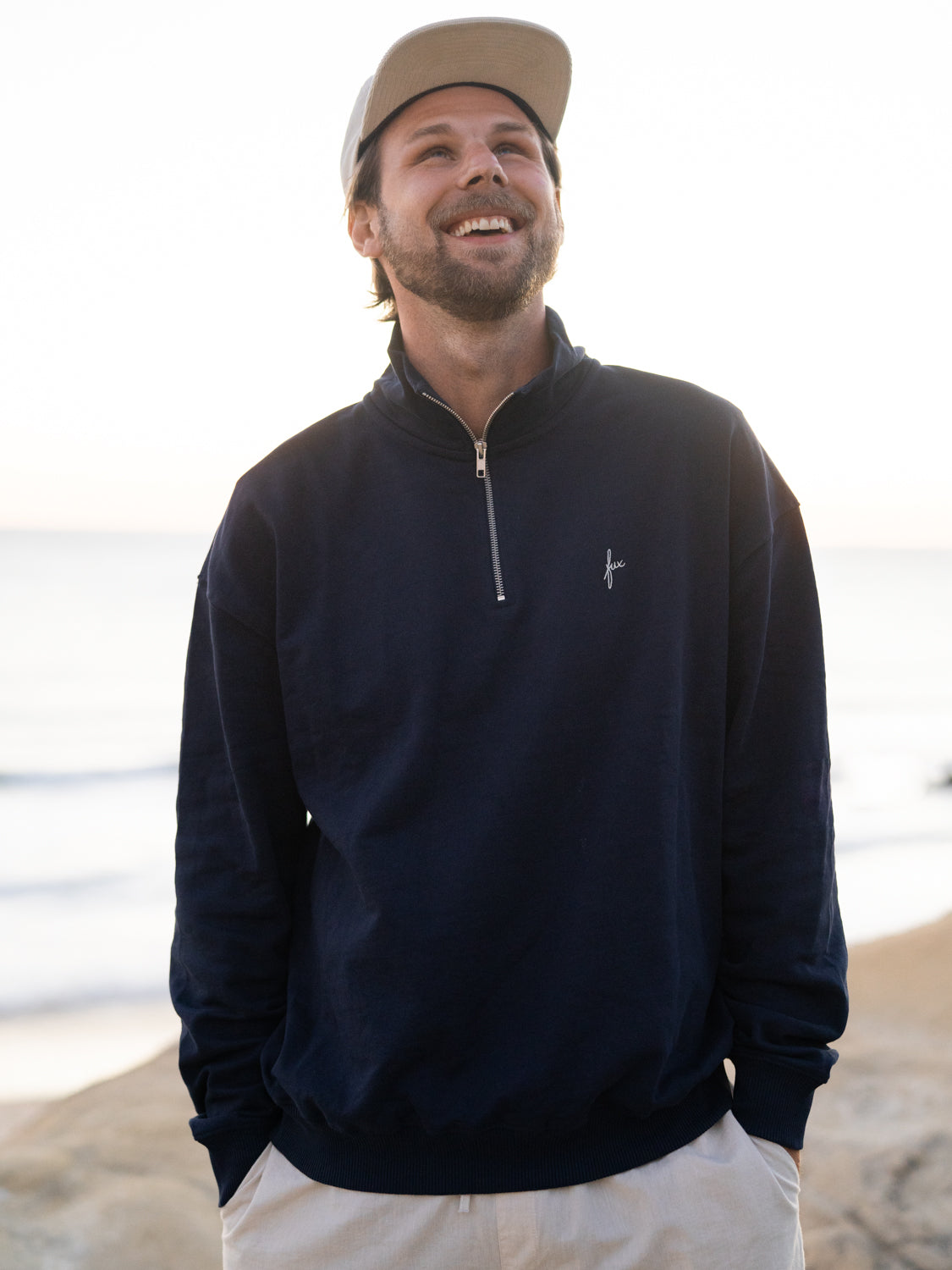 Nachhaltiger Half Zip Sweater in navy von FUXBAU aus Biobaumwolle getragen am Strand von Philipp in Spanien.