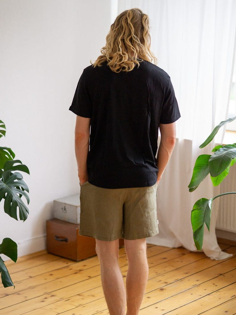 Rückansicht von unserem Freund Mo, der das Fair Fashion Schweres Basic T-Shirt in schwarz von FUXBAU aus 100% Biobaumwolle trägt.