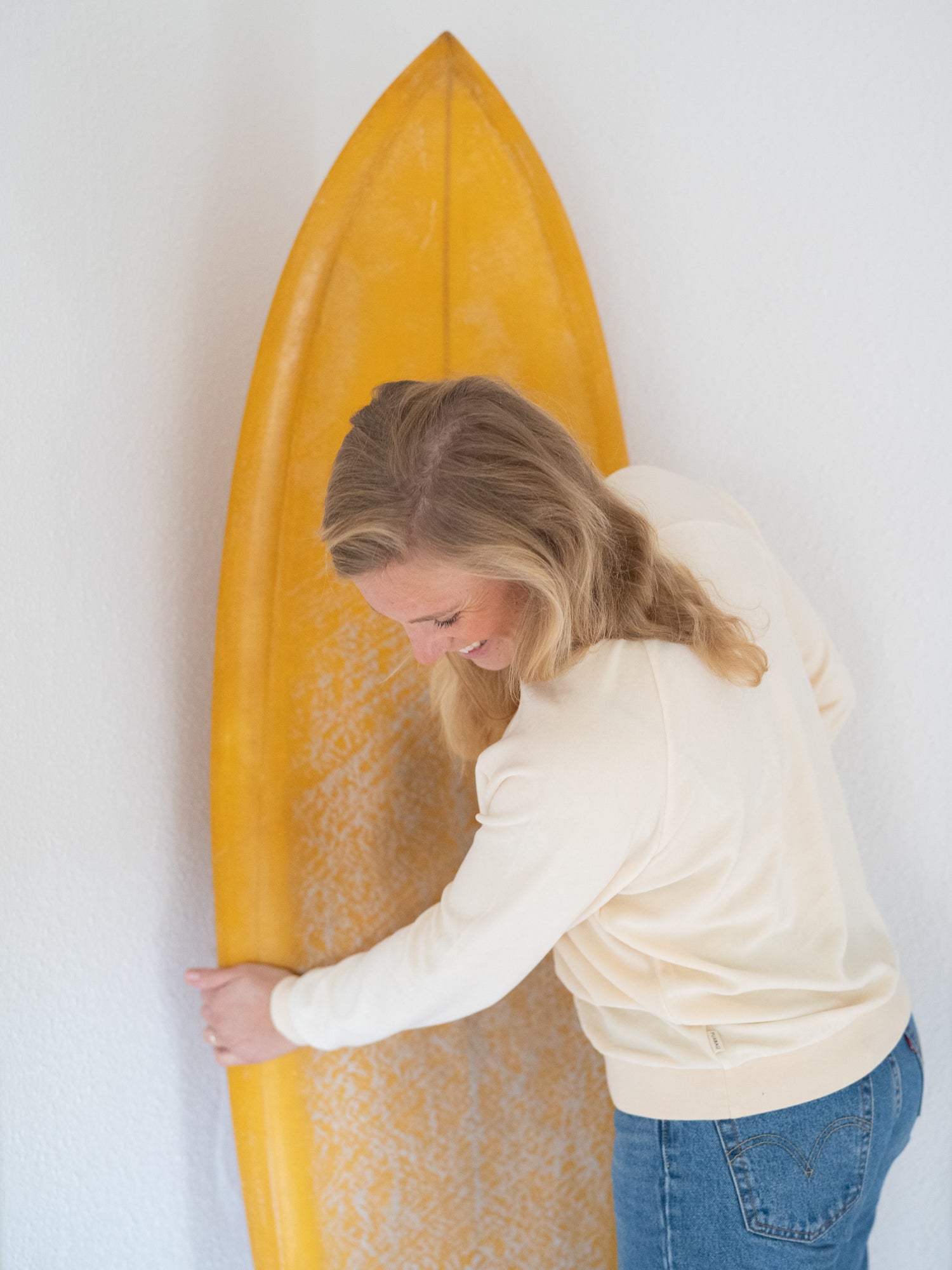 Isi trägt unseren FUXBAU Fair Fashion Frauen Samt Pullover in weiss aus Leftover Fabrics made in Portugal und hält ein Surfbrett in der Hand