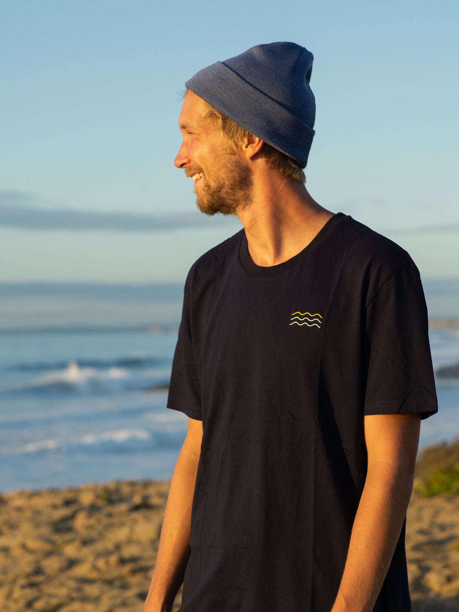 Kenny trägt unser FUXBAU Fair Fashion Surf T-Shirt in navy aus Biobaumwolle am Meer