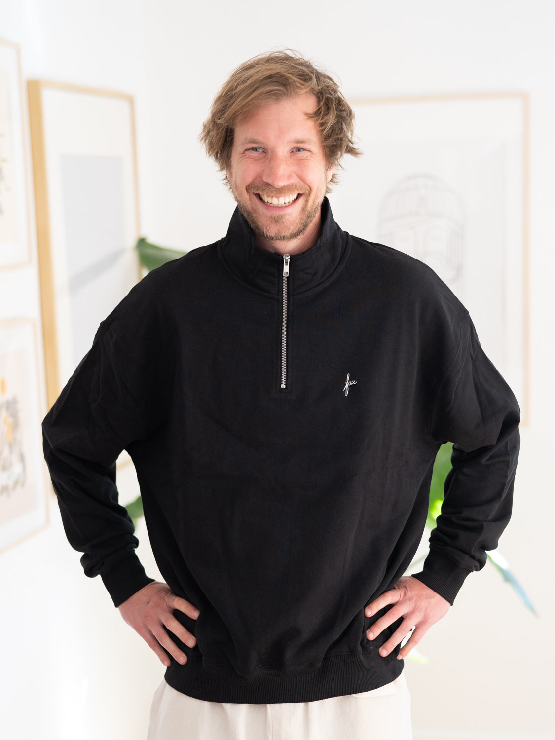 Kenny trägt unseren FUXBAU Fair Fashion Half Zip Sweater in schwarz aus Biobaumwolle