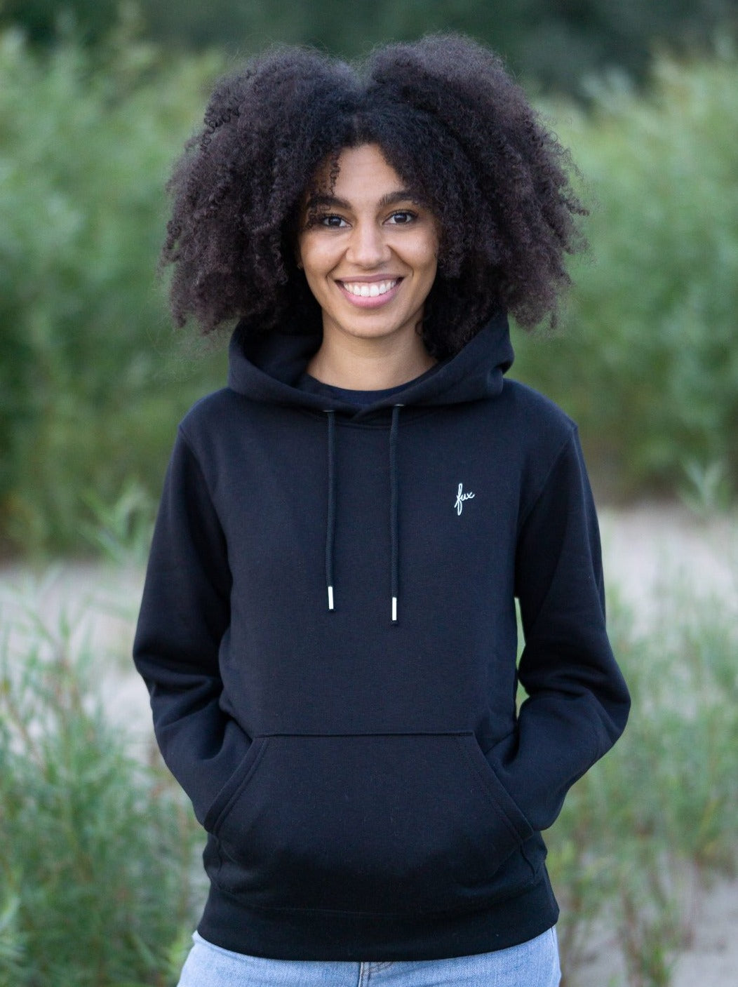 Junge, schwarzhaarige Frau trägt einen fairenund nachhaltigen Hoodie von FUXBAU in schwarz. 